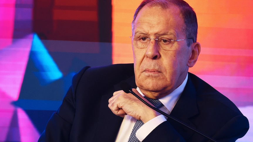 Sergei Lavrov shown in a tight shot wearing a terse expression with a bright projected pattern in the background