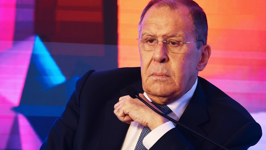 Sergei Lavrov shown in a tight shot wearing a terse expression with a bright projected pattern in the background