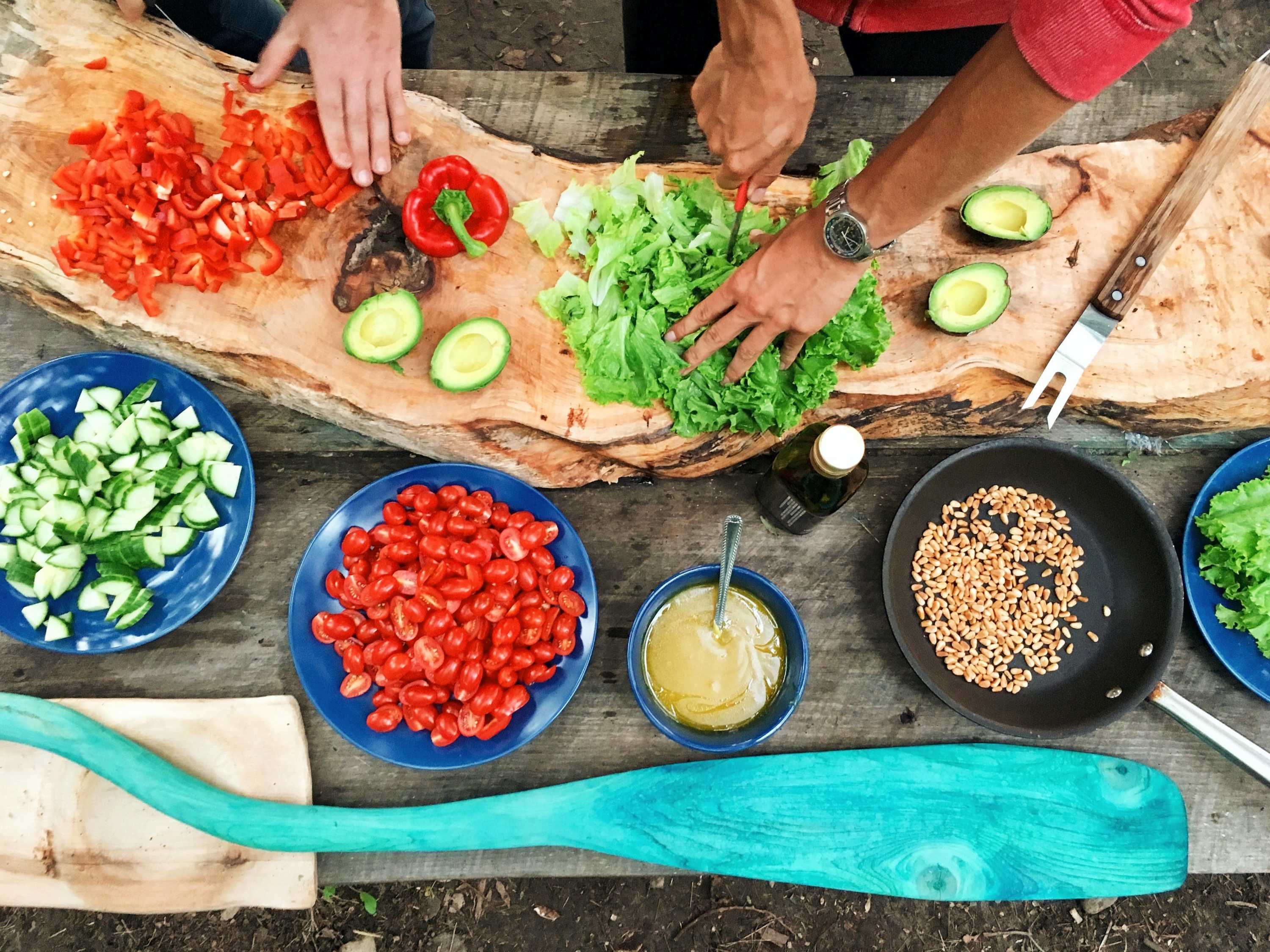 Hands chopping vegetables on a long wooden board.
