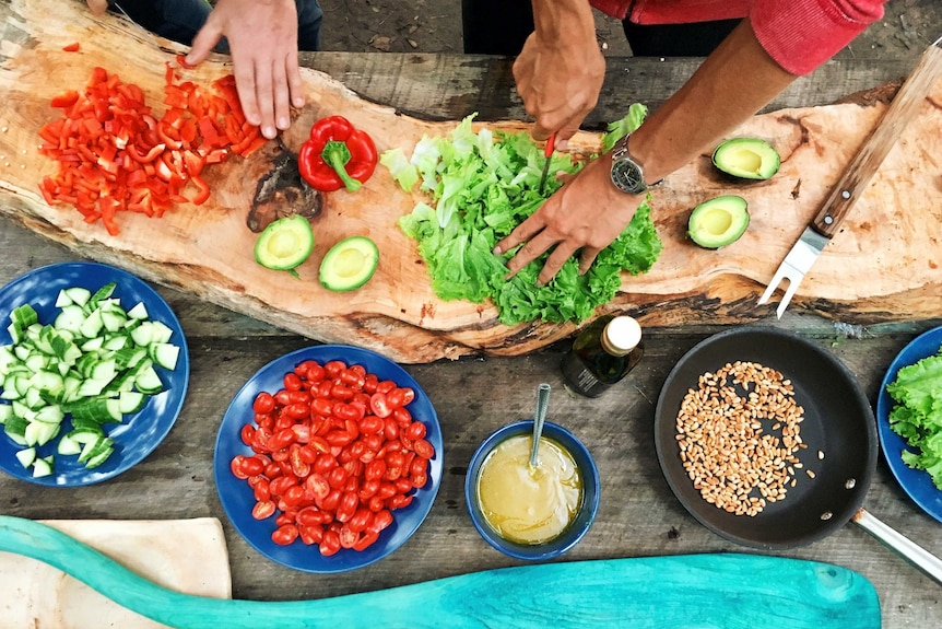 Hands chopping vegetables on a long wooden board.