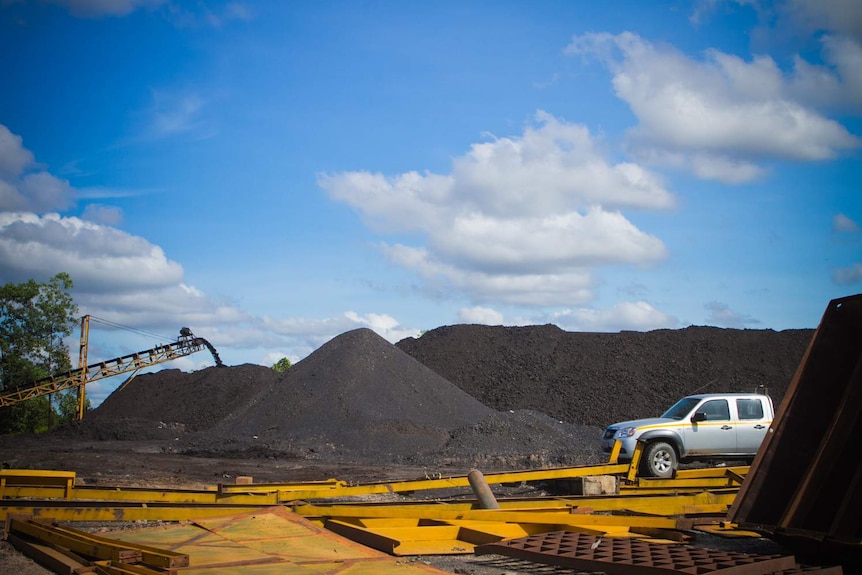 Mounds of coal with a crane to the left and a silver car to the right.