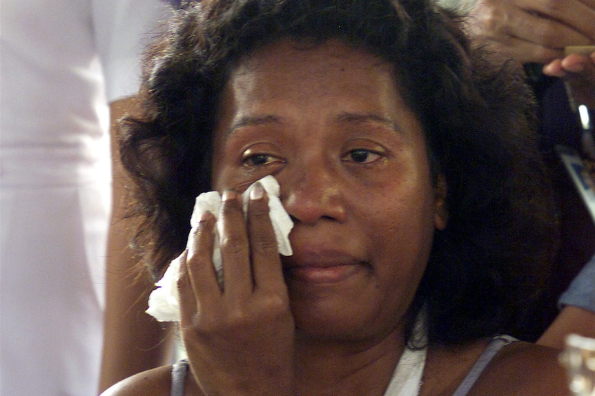 A woman with short black hair dries her eyes with a tissue as she cries.