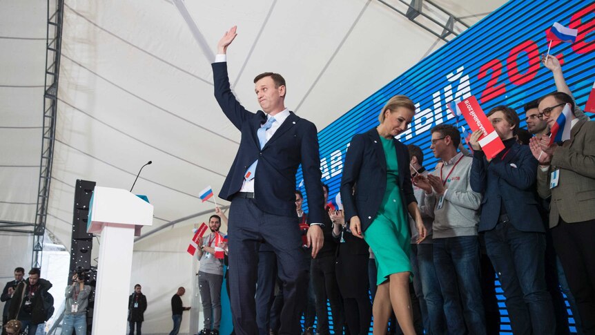Alexei Navalny waves to his supporters and his wife walks next to him.