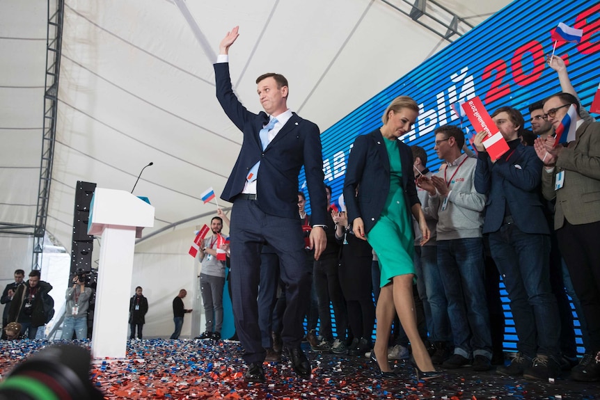 Alexei Navalny waves to his supporters and his wife walks next to him.