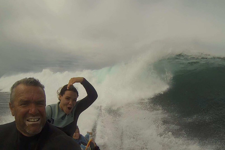 A man on a jet ski with his two kids in the background riding down a huge wave.
