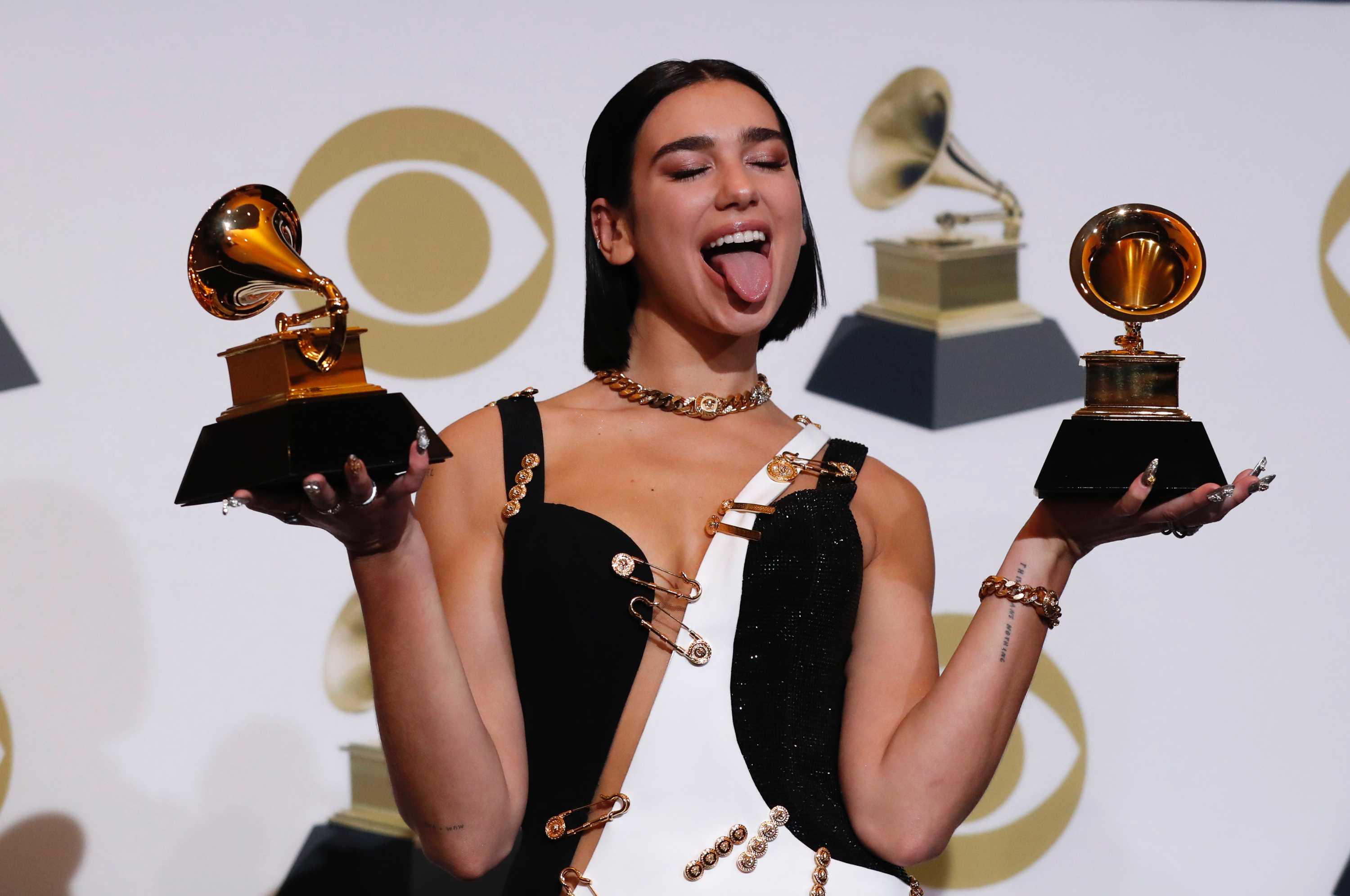 Pop star Dua Lipa makes a silly face for the cameras while holding two Grammy awards in front of a media backdrop