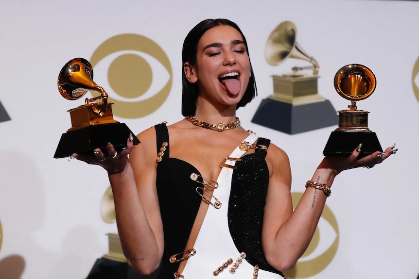 Pop star Dua Lipa makes a silly face for the cameras while holding two Grammy awards in front of a media backdrop
