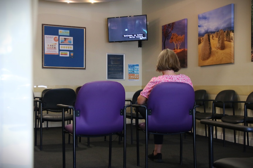 Woman with bob haircut sits on a purple chair in an empty doctor waiting room.