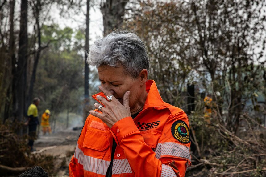 A woman in tears in a high-vis jacket standing outside.