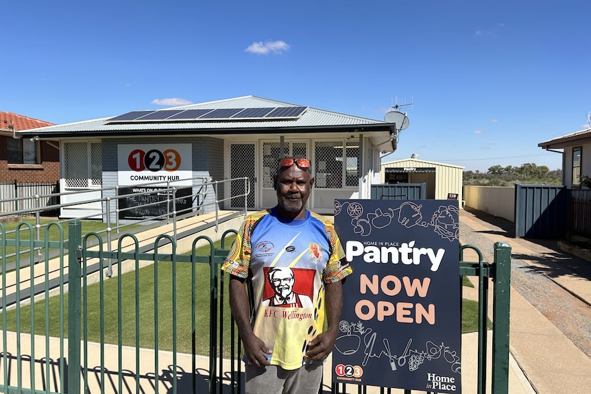 An Indigenous man stands in front of a building next a sign saying The Pantry 