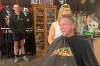 A man at a barber shop, getting a mullet hair cut