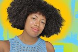 Yasmin smiles as she looks to the camera in a selfie, with her short afro out, standing in a kitchen coloured blue and yellow.