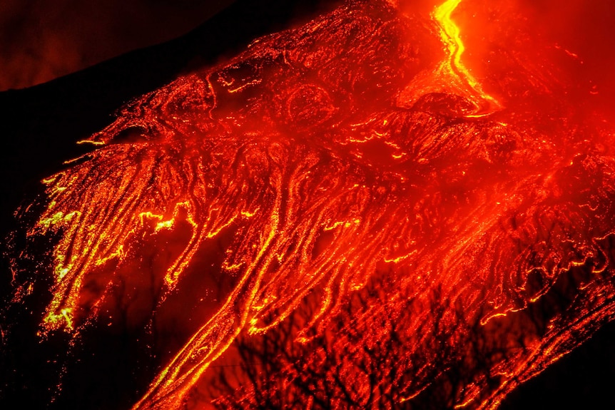 A close up of a mountain erupting at night with red hot lava shooting up.