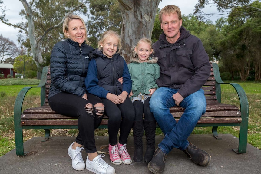 The Squires family, Danielle, Olivia, Zoe and Daryl sit on a park bench and smile at the camera.