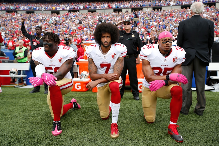 Three San Francisco 49ers players kneel during the US national anthem before an NFL match.