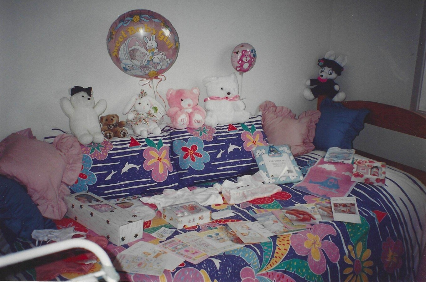 ஸ்டஃப் செய்யப்பட்ட கரடிகள், பலூன்கள் மற்றும் குழந்தை ஆடைகள் மேல் ஒரு படுக்கை. 