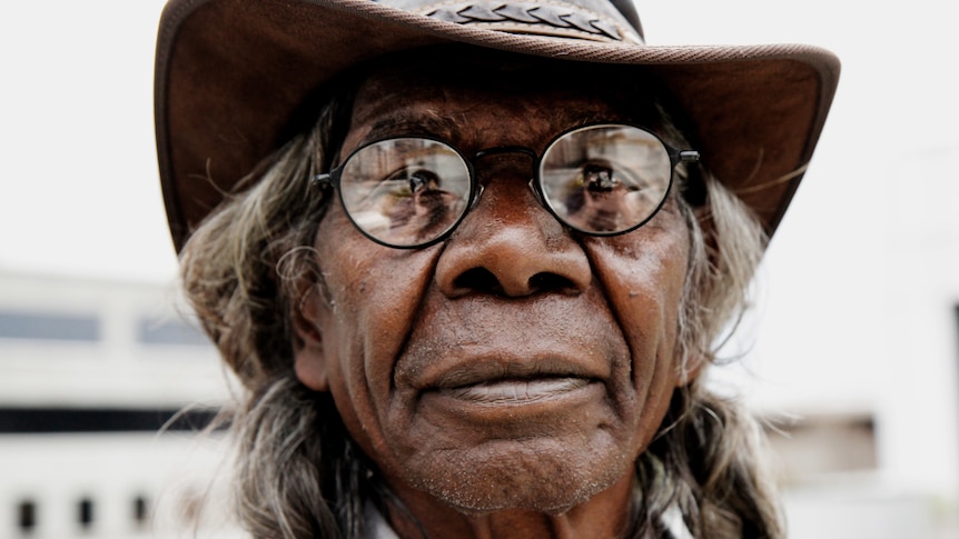 A portrait shot of David Dalaithngu wearing glasses and a hat.