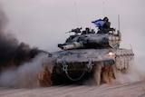 A soldier holds an Israeli flag while riding on a tank through the desert.
