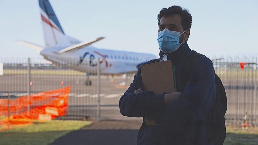 A man wearing a mask stands at the Mount Gambier Regional Airport terminal entrance after disembarking from aircraft