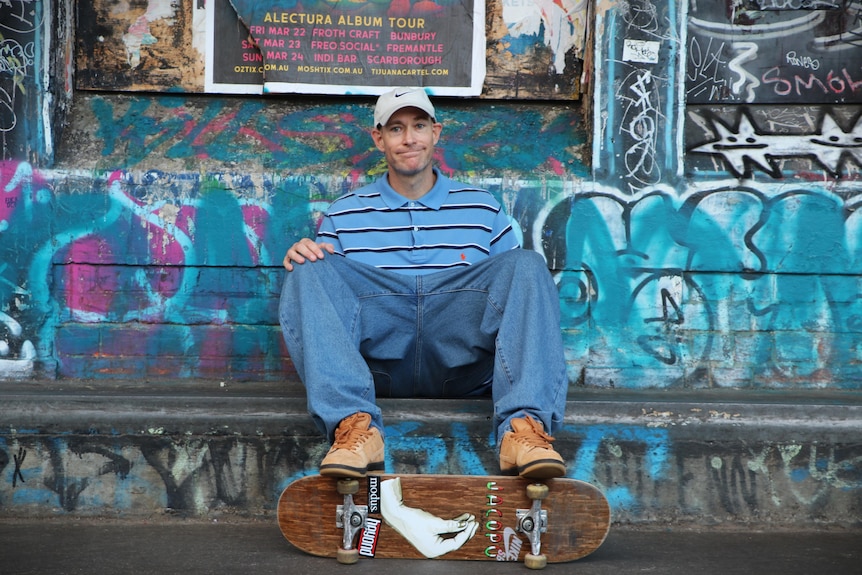 A man named Ben Bowring sitting with his feet on a skateboard.