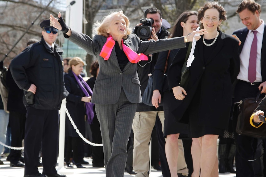Edith Windsor walks with her arms outstretched looking joyful.