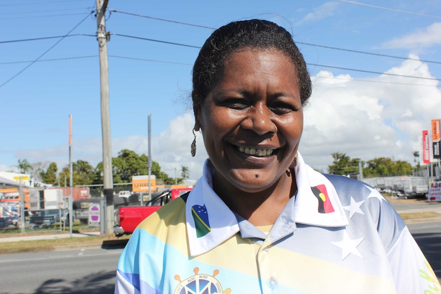 A woman wearing a shirt with the South Sea Islands and Australian Aboriginal flags smiles