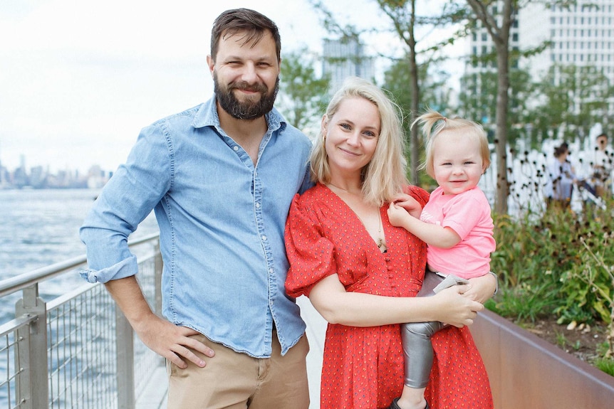 A woman stands next to a man and holds a small child.