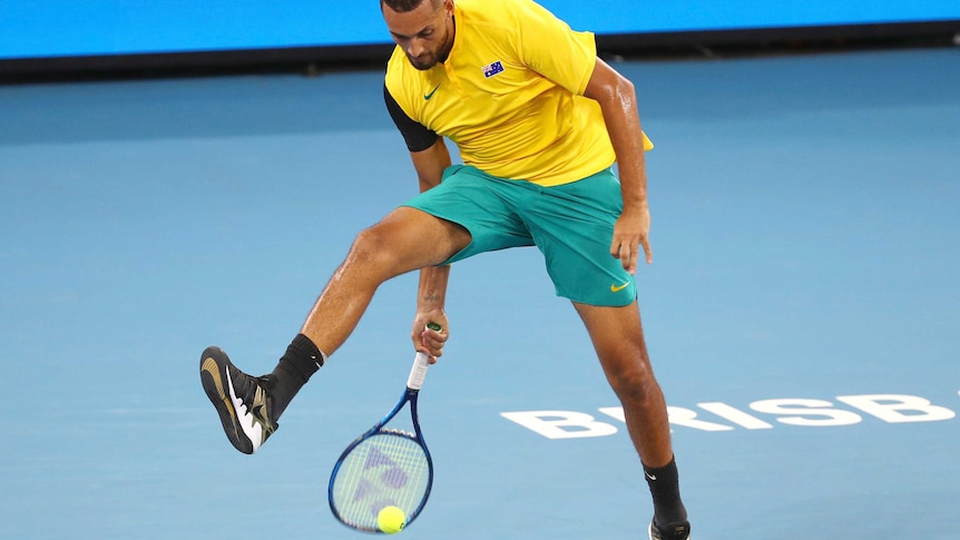 A tennis player plays a shot through his legs mid-air.
