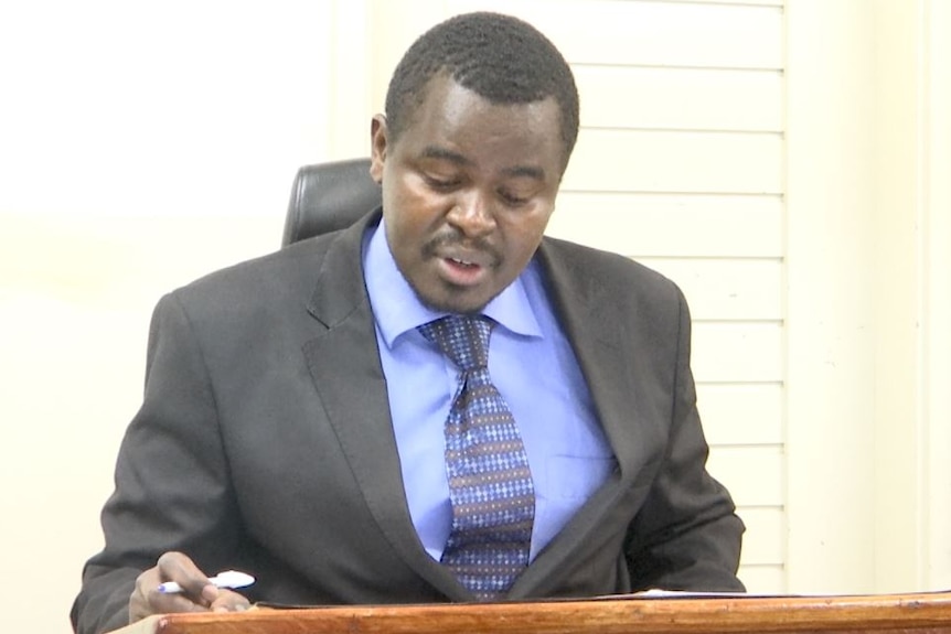Magistrate Derrick Khaemba Kuto holds a pen in his hand in court and looks down at paperwork.