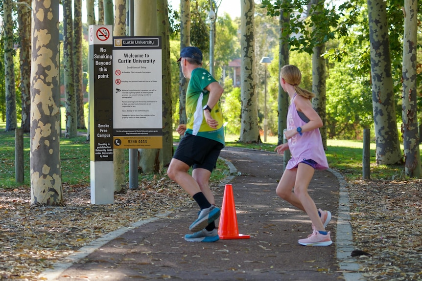 A man and young girl run around a witch hat while doing parkrun.
