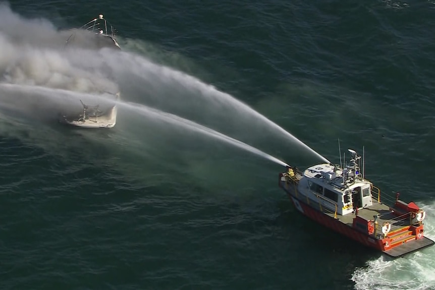 A boat spraying water on another boat which is alight