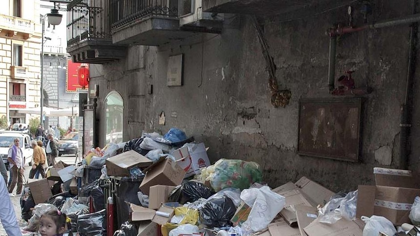 Pedestrians walk by uncollected garbage in downtown Naples