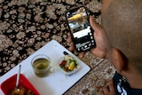 Interior scene over shoulder image of a man eating lunch watching video on his phone