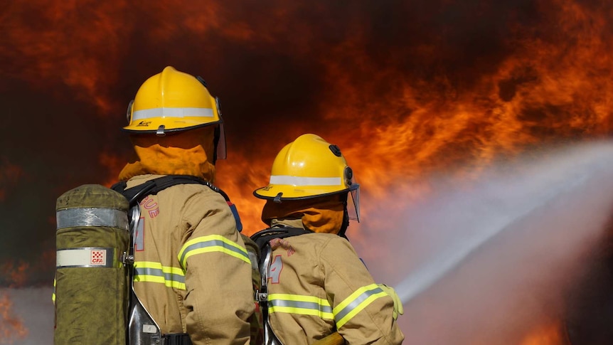 Two CFA firefighters holding a hose against a wall of fire