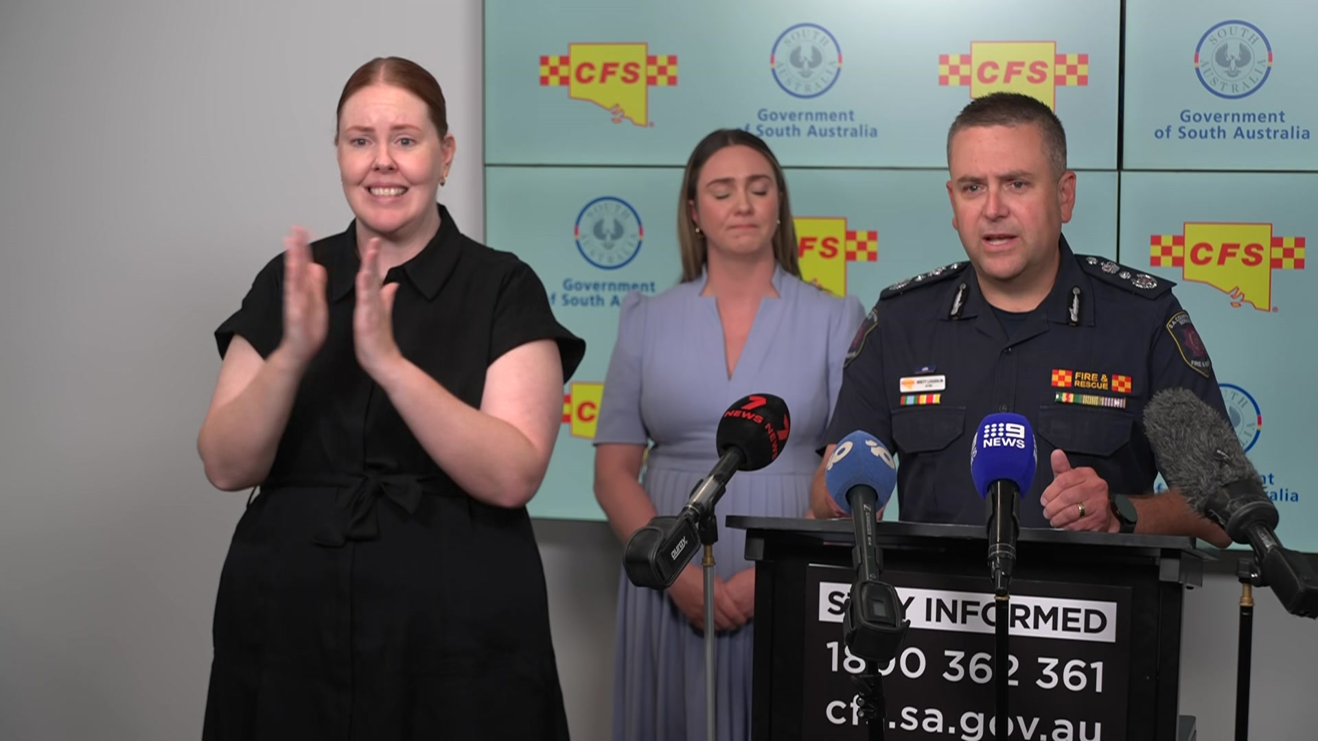 Um homem fala em uma coletiva de imprensa com um intérprete surdo e outra mulher atrás dele