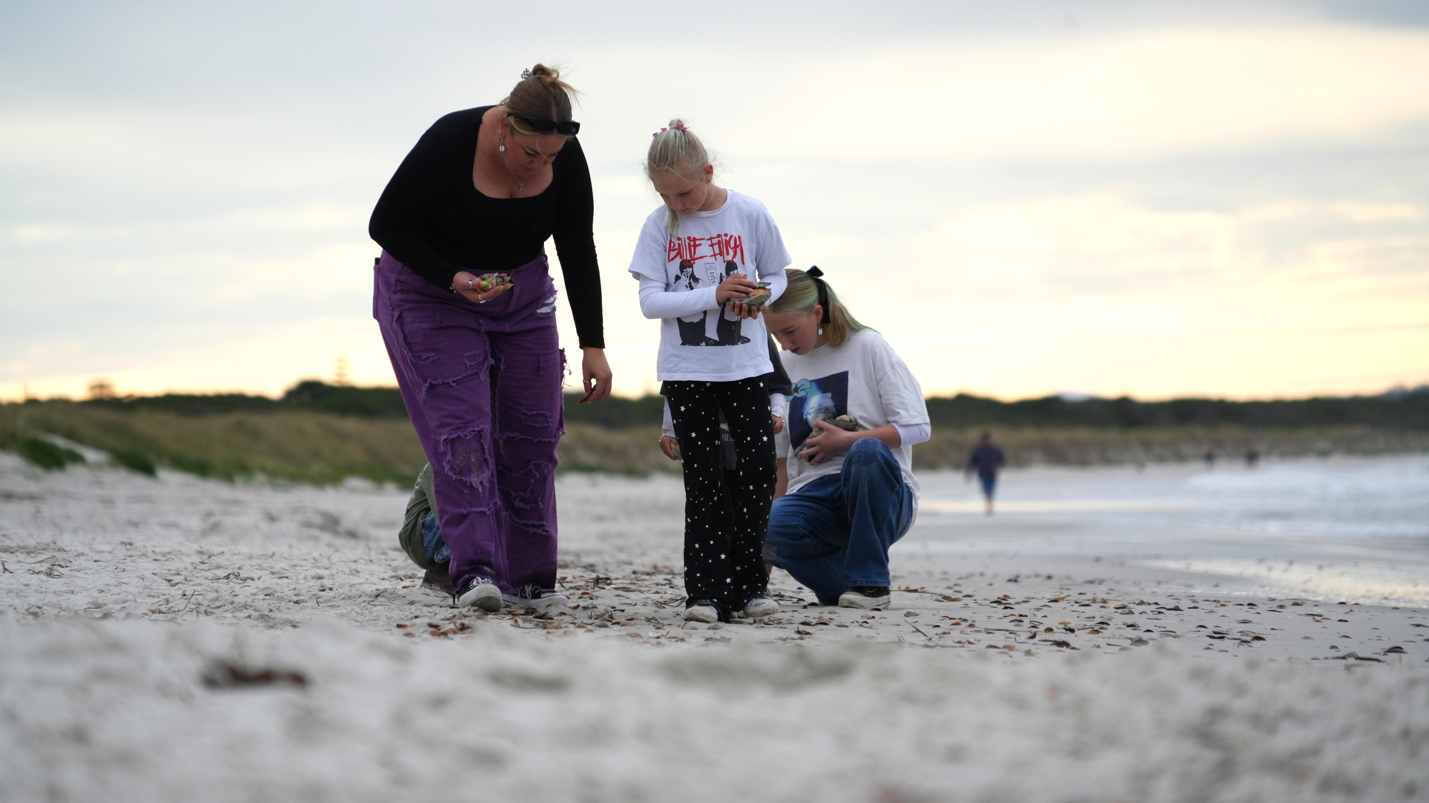 A woman and two girls look for shells on the beach.