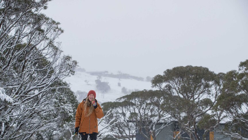 A smiling woman stands in thick snow on a mountain-side, holding a snow ball.