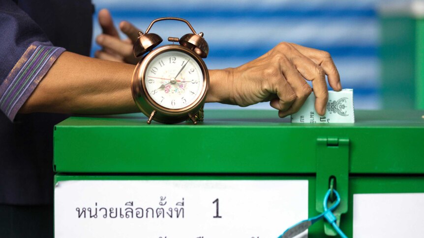 A close up of a green ballot box and a hand casting a vote. Old-fashioned clock sitting on top.