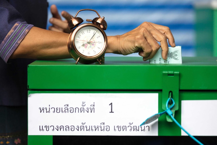 A close up of a green ballot box and a hand casting a vote. Old-fashioned clock sitting on top.