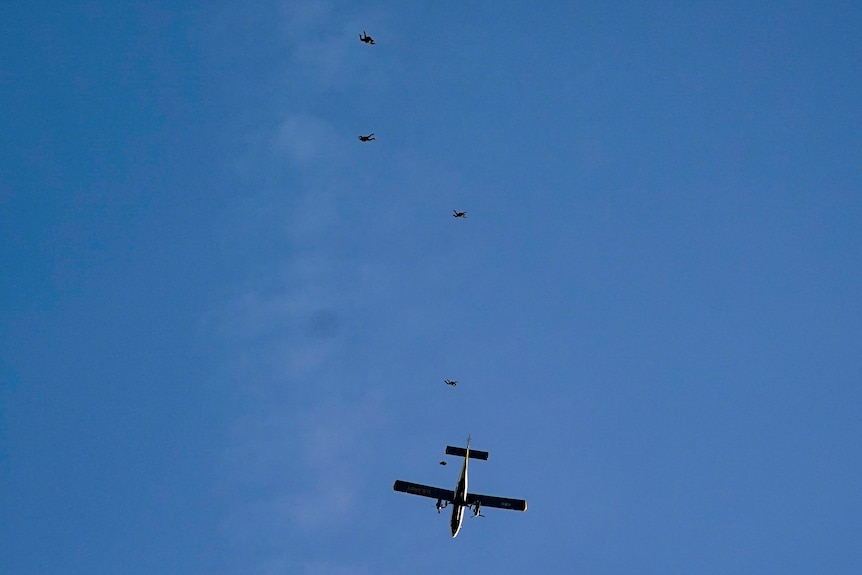 A view from the ground of parachutists jumping out of a twin-engined plane.