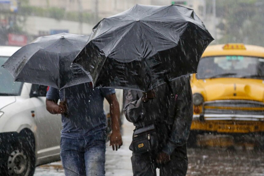 Two men hold umbrellas in the wind and rain.