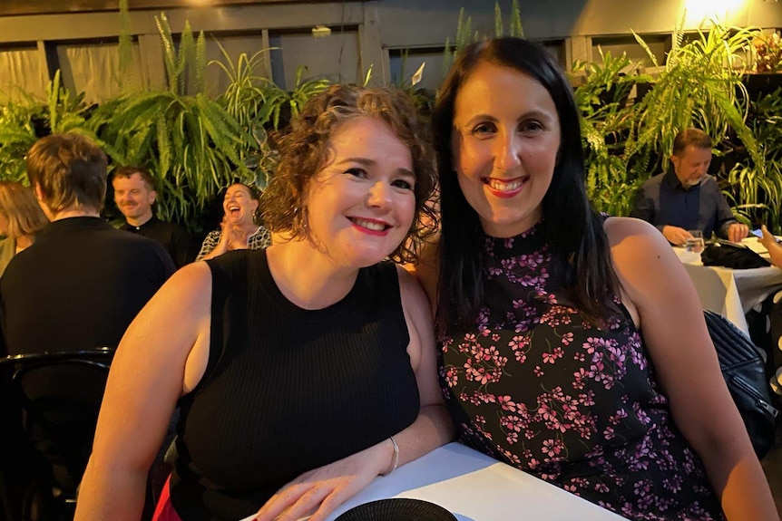 Two woman smiling and looking at the camera while out with friends at a restaurant