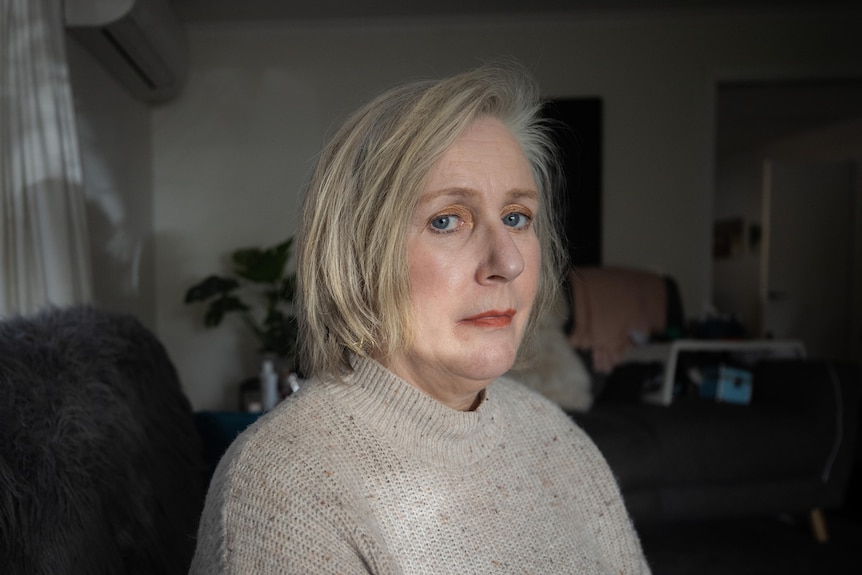 Woman with blonde hair sits in a dark room looking sad 