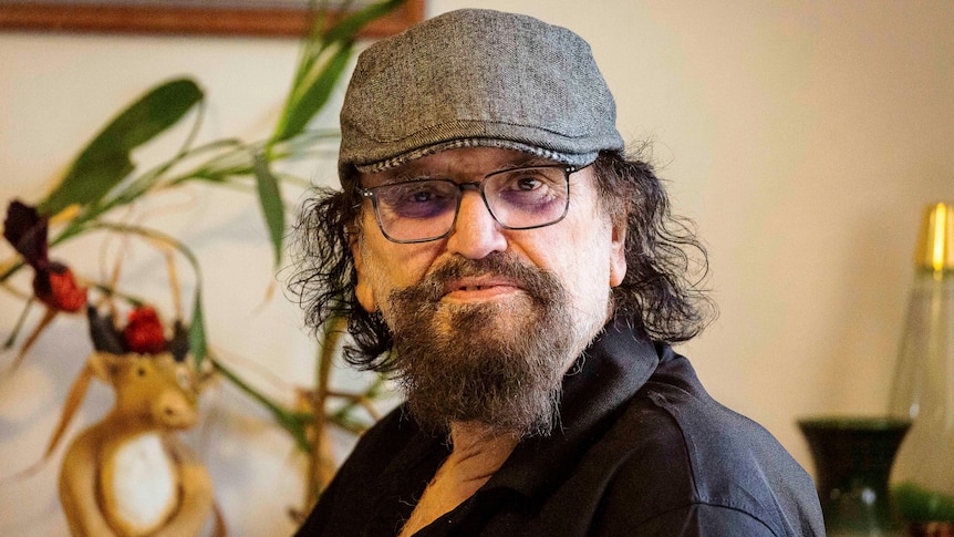 A man wearing a black cap, glasses and a black shirt looking into the camera.