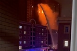 Firefighters spray water on fire at tall apartment building.