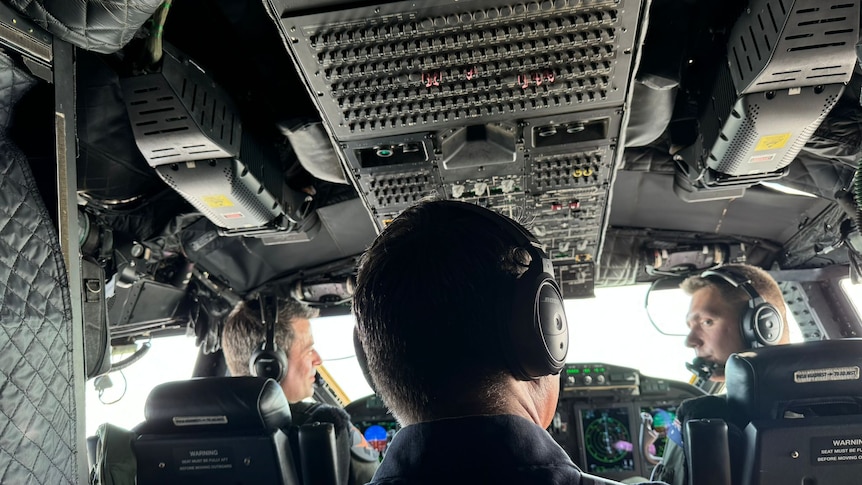 The back of Richard Marles's head as he sits in the cockpit of a helicopter with two pilots.