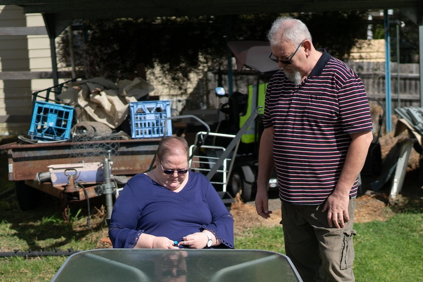 Woman sitting at table in back garden with man standing next to her