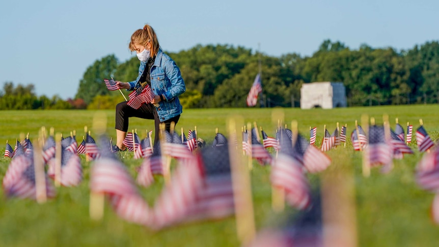 A woman in a mask kneels in a field of US flags