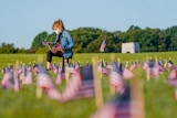 A woman in a mask kneels in a field of US flags