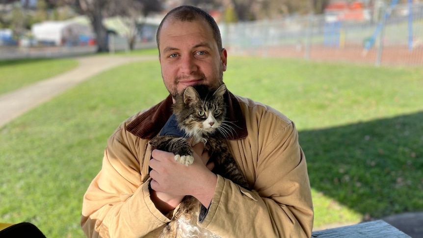 A man holds a tabby cat and smiles